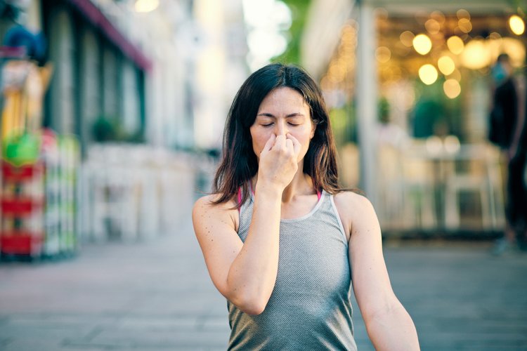 Persona con occhi chiusi e mano sul naso che pratica la respirazione alternata, all'aperto in ambiente urbano