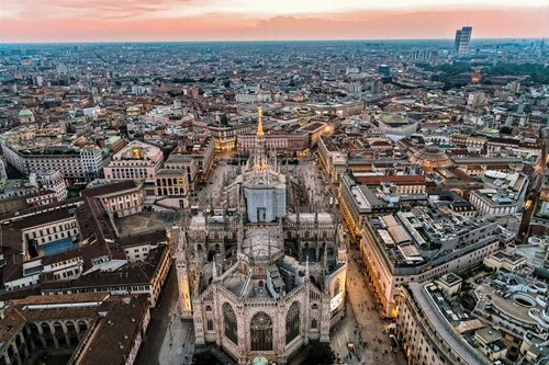Milano dall’Alto – Duomo al Tramonto, 5 cose da fare ad agosto Veduta aerea del Duomo di Milano al crepuscolo: guglie illuminate e skyline che si perde all'orizzonte