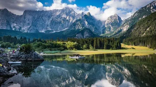 Lago alpino con perfetto riflesso di cime innevate e foreste di conifere, con imbarcazioni sulla riva