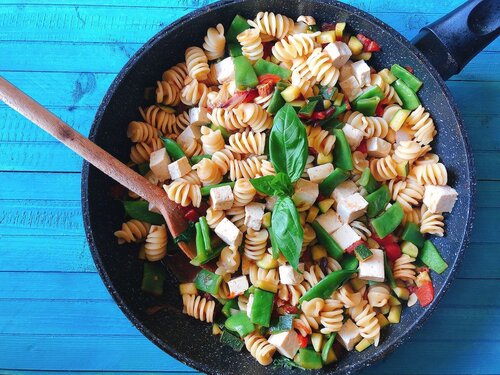 Il Piatto Estivo Perfetto in 5 Step – Pasta con Verdure Padella con fusilli, fagiolini, foglie di basilico e cubetti di formaggio bianco su un tavolo azzurro