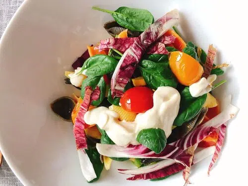 Insalata colorata in ciotola bianca con spinaci, radicchio, pomodorini colorati, mozzarella e aceto balsamico