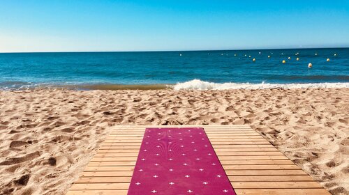 Tappetino Yoga Rosa su Pontile di Legno – Mare e Spiaggia Tappetino yoga rosa fucsia su pontile di legno che si affaccia su spiaggia sabbiosa e mare blu