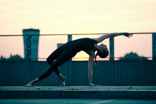 Silhouette in camatkarasana sul tetto di un edificio urbano al tramonto con skyline della citt&agrave; sullo sfondo
