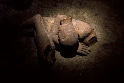 Scultura in terracotta di figura umana accovacciata e addormentata, illuminata dall