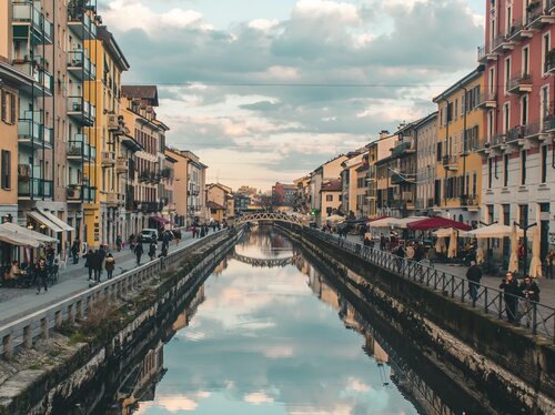 Navigli Milano – Canale storico nella città dei 15 minuti Canale dei Navigli a Milano con edifici colorati che si rispecchiano nell'acqua, passanti e un ponte sullo sfondo