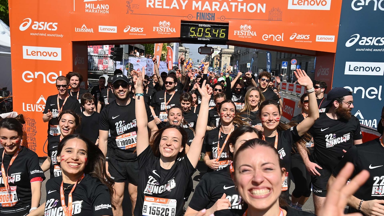 Gruppo di runner in maglietta nera esulta sotto l'arco del traguardo della Milano Marathon Relay
