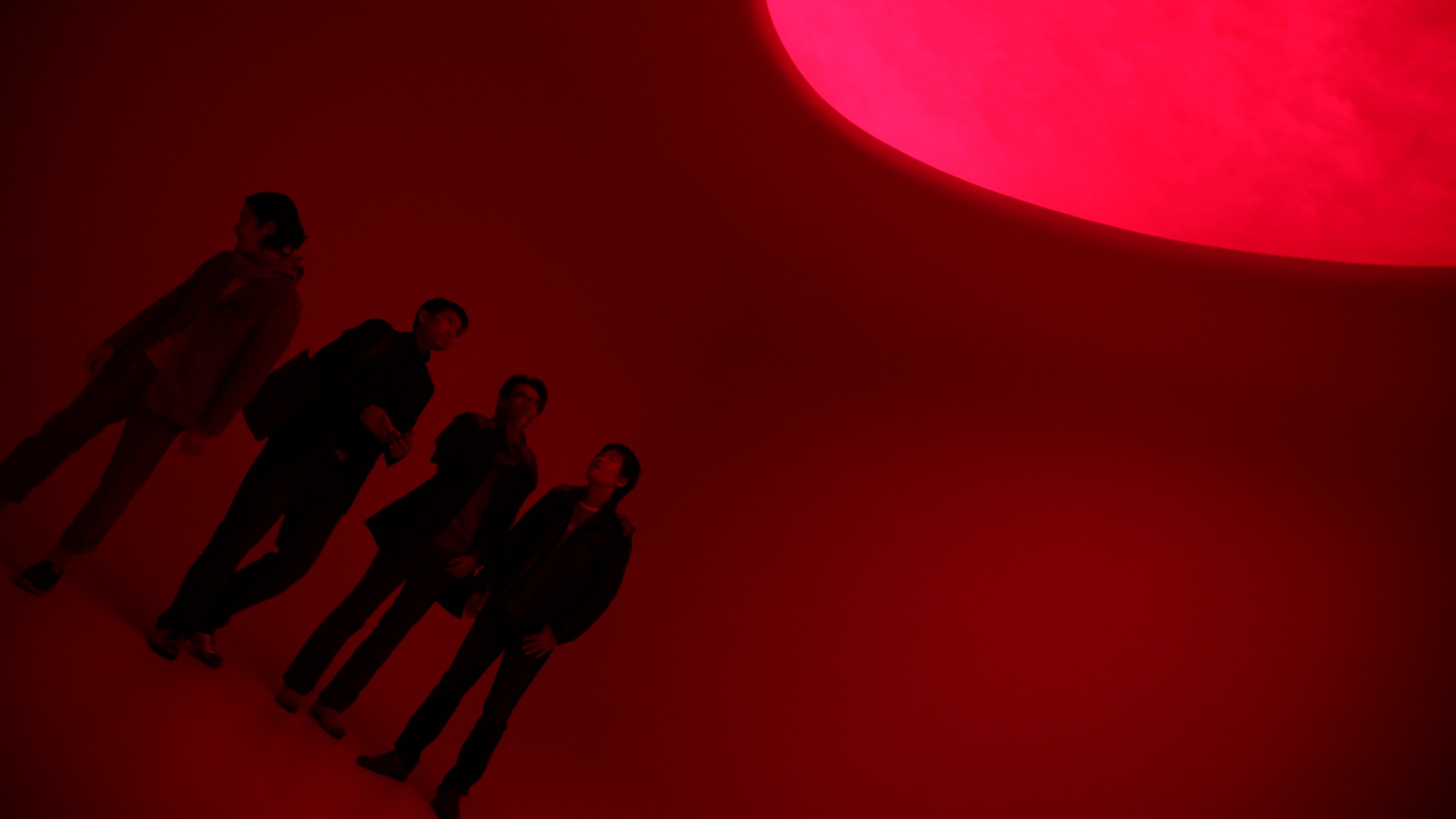 Installazione immersiva rossa con visitatori in controluce e grande forma curva luminosa