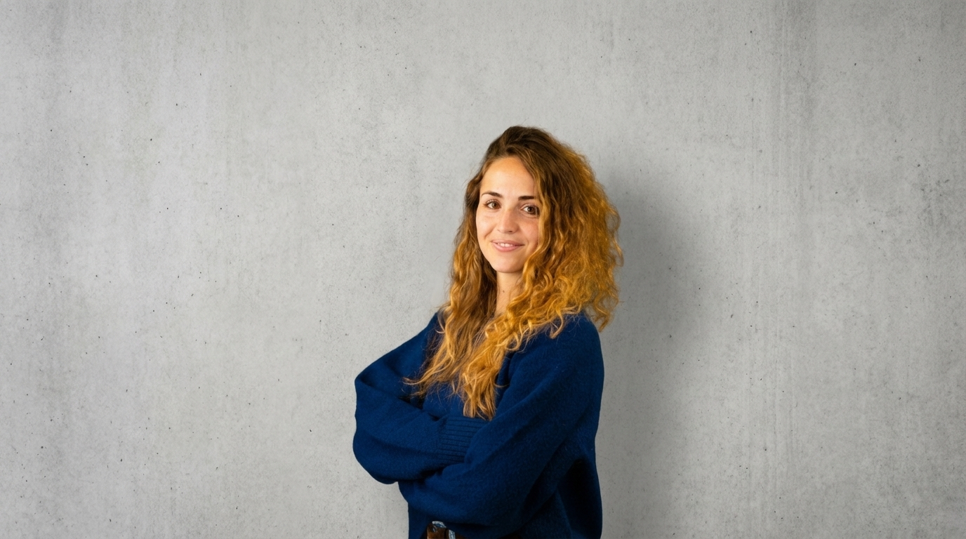 Insegnante di Milano Yoga Space con capelli ricci e giacca blu, braccia conserte, su sfondo in cemento
